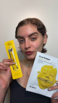 En gul plastapplikator och förpackning för Cryo Rubber ansiktsmask med en blank gul ansiktsgrafik och silveraccent på applikatorn.