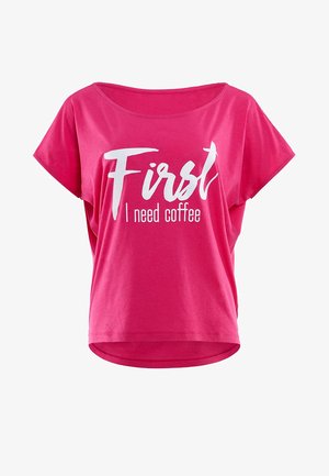 Fuchsias kortärmad T-shirt i bomull. Har en bred halsringning och vit text som säger "Först behöver jag kaffe" i lekfulla typsnitt.