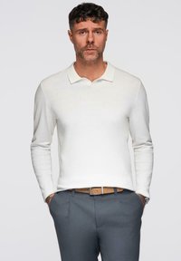 Witte longsleeve polo met een vlakke kraag, gedragen met grijze dresspants en een tan riem. Eenvoudige, geweven stof met minimale details.