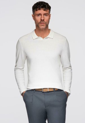 Witte longsleeve polo met een vlakke kraag, gedragen met grijze dresspants en een tan riem. Eenvoudige, geweven stof met minimale details.