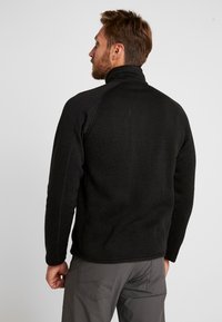 Schwarzer Fleece-Pullover mit hohem Kragen, strukturiertem Stoff und abgesetzten Nähten. Raglanärmel und schmaler Schnitt. Leicht und flexibel.