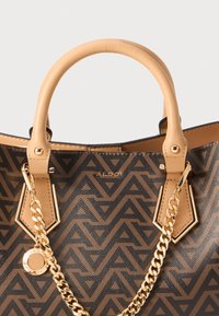 Sac à main brun à motifs avec des poignées beiges lisses, un détail en chaîne dorée et un logo proéminent. Présente un design géométrique sur un matériau durable.