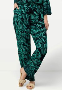 Svarta byxor med ett grönt lövmönster, tillverkade av ett lättviktigt tyg, med dragsko i midjan och en texturerad fåll.