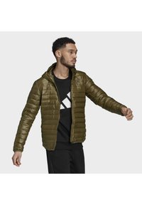 Doudoune vert olive avec un design ajusté, texture matelassée horizontale et une capuche. Comprend une fermeture éclair à l'avant et un logo sur la poitrine.
