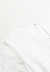 Vit plagg med texturerad tyg, som har spetsärmar och en knappstängning bak. Slät yta med känsliga blommönster.