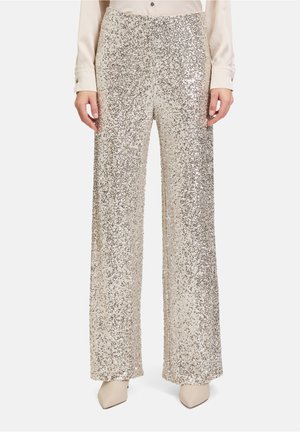 Pantalons larges recouverts de sequins argentés, mettant en valeur une texture étincelante. Assortis à un chemisier crème et des talons beiges.