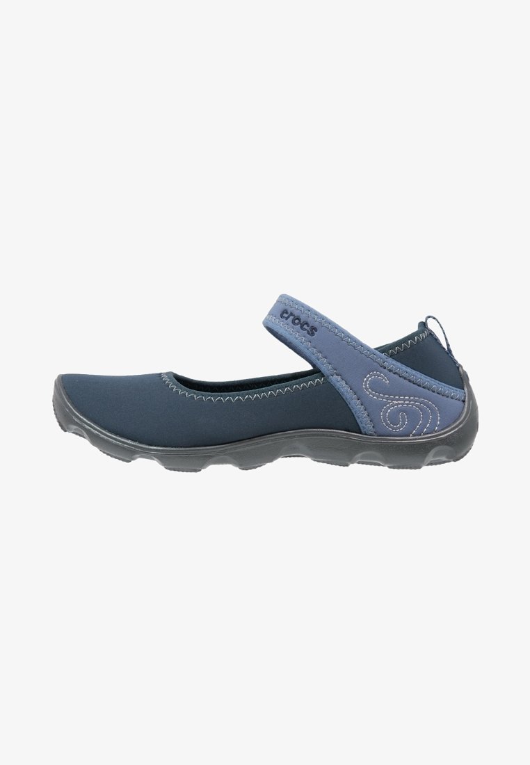 Zapato slip-on en azul marino con parte superior de tela suave, tira elástica y suela gris texturizada. Presenta costuras curvas y detalles del logo.