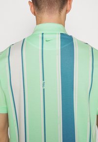 Polo shirt vert menthe avec des rayures verticales dans différentes nuances de vert et de bleu, avec un col discret et un petit logo dans le dos.