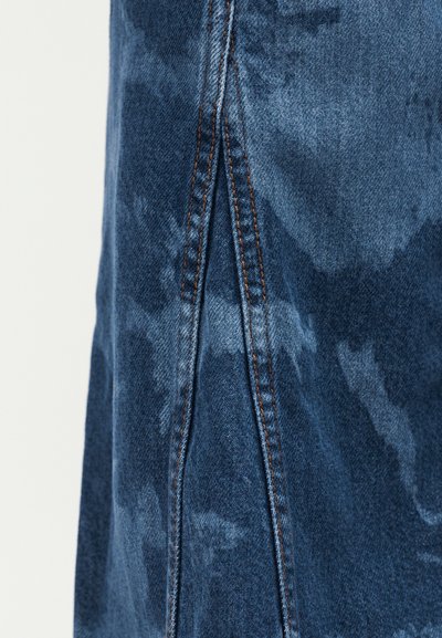 Σκούρο μπλε τζιν ύφασμα με διπλή πορτοκαλί ραφή κατά μήκος μιας κεντρικής ραφής και τριγωνική λεπτομέρεια επικάλυψης.