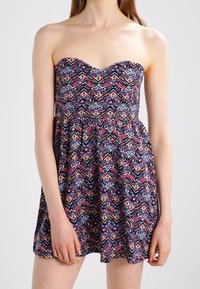 Robe sans bretelles avec un motif floral et géométrique, comportant des nuances de violet, rose et bleu, avec une jupe évasée et texturée.