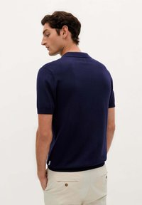 Mørkeblå kortærmet polo shirt lavet af et blødt, glat materiale, med en klassisk krave og en let sideslids i kanten for komfort.