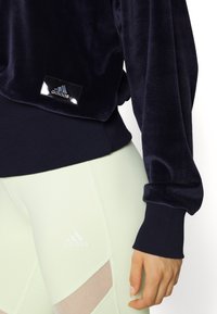 Sweat-shirt en velours bleu marine avec poignets et ourlet côtelés ; orné d'un patch logo noir brillant. Complété par des leggings vert clair avec des accents en mesh.