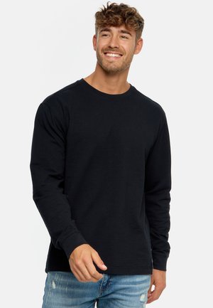 Schwarzes Langarm-T-Shirt mit gerippter Textur, Rundhalsausschnitt und schmalen Bündchen, kombiniert mit ausgebleichten blauen Jeans.