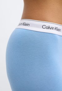 Ανοιχτό γαλάζιο βαμβακερό εσώρουχο με φαρδιά λευκή ελαστική μέση που φέρει την επιγραφή «Calvin Klein» μαύρα γράμματα. Λείο υλικό, εφαρμοστή σχεδίαση.