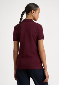 Μπλούζα πόλο μπορντό με κλασικό γιακά, κοντά μανίκια και αντίθετες σκουρόχρωμες μανσέτες, συνδυασμένη με ναυτικό μπλε παντελόνι τύπου cargo. Ομαλή υφή υφάσματος.