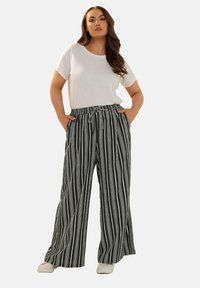 Svartvita randiga löst sittande byxor med elastisk midja och dragsko, kombinerade med en enkel vit t-shirt och beige skor.