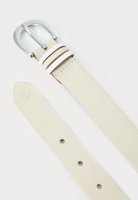 Beige leren riem met zilveren dubbele haakgesp. Heeft witte en bruine strepen nabij de gesp. Gevarieerde textuur, vijf verstelgaten.