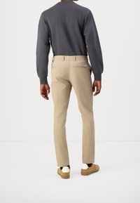 Beiga chinos med slim fit och detaljer på bakfickan, i kombination med en mörkgrå långärmad topp och ljusbruna skor. Slät textur.