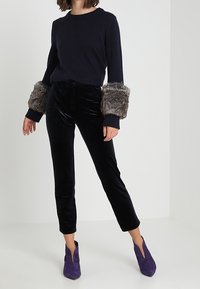 Maglione lavorato a maglia blu navy con polsini in pelliccia, pantaloni in velluto nero e stivaletti viola con tacco. Caratterizzato da tessuto strutturato e vestibilità sartoriale.