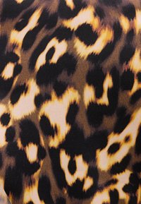 Κοντινό πλάνο υφάσματος με καφέ, μαύρο και μπεζ μοτίβο λεοπάρδαλης που δείχνει ακανόνιστα σημεία και μπαλώματα.