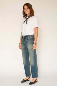 T-shirt blanc, jean taille haute bleu, ballerines noires avec découpes. Le mannequin porte une écharpe noire ; le fond est de couleur neutre.