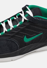 Baskets Nike noires et vertes en matériaux maille et daim, avec des lacets blancs et un logo swoosh vert bien en évidence sur le côté.
