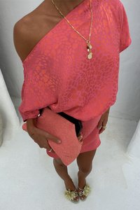 Top overdimensionato con stampa leopardata rosa abbinato a una gonna corta coordinata. Gli accessori includono una pochette rosa texture e sandali con dettagli pom-pom.