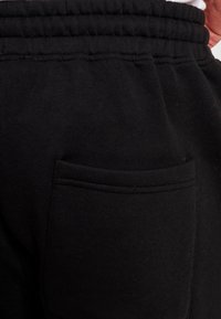 Schwarze Sweatpants aus strukturiertem Stoff, mit elastischem Bund und einer flachen Tasche auf der rechten Seite.