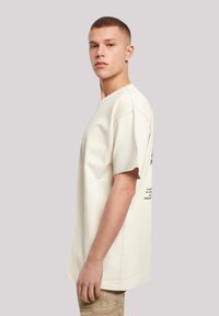 Cream-colored short-sleeve t-shirt with a relaxed fit. Features a printed graphic on the back and stitching details on the shoulders.