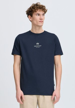 Mørkeblå bomull T-skjorte med en liten hvit logo på brystet. Korte ermer og rund hals. Glatt tekstur, klassisk passform.