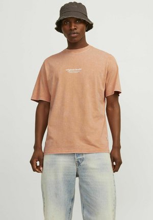 Lyserød bomulds t-shirt med korte ærmer og rund halsudskæring, med et lille hvidt logo på fronten. Bærer sammen med slidte blå jeans.