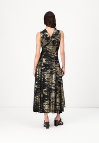 Rochie lungă cu imprimeu negru și auriu, cu un corset ajustat, mâneci scurte, spate în formă de V și fustă fluidă. Asortată cu sandale negre cu toc pătrat.