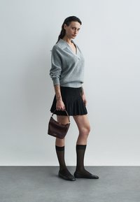 Szary sweter z dzianiny, czarna rozkloszowana spódnica, przezroczyste czarne pończochy, czarne baleriny oraz ciemnoczerwona torebka z złotymi akcentami. Prosty, nowoczesny design.