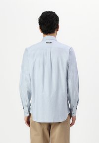 Camicia a maniche lunghe blu chiaro e bianca a righe con polsini abbottonati, piega sulle spalle e orlo dritto, realizzata in un tessuto liscio.