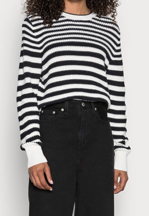 Pull en tricot à rayures noir et blanc avec des manches longues, doté de bords côtes aux poignets et d'un col rond ; associé à un jean noir taille haute.