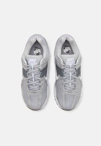 Grå träningsskor med en mesh-övre, kontrasterande grå overlay och en vit swoosh-logotyp. Har en rund tå och snörning.