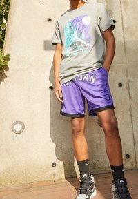 Gray graphic T-shirt featuring a basketball design, paired with purple mesh shorts with "JORDAN" text, black trim, and black Nike socks.