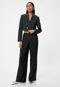 Blazer gris cortado de doble botonadura con botones metálicos, combinado con pantalones negros de cintura alta y tacones plateados de punta.