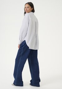 Light striped shirt with a loose fit and pleated back detail, paired with dark blue wide-leg jeans. Smooth fabric and soft texture.