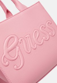 Sac à main en simili cuir rose avec logo "Guess" en relief, couture soignée et doubles anses. Texture lisse et forme rectangulaire.