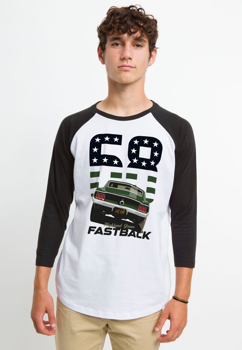 Baseball T-shirt med hvid krop og sorte raglanærmer. Har grafik af en bil, teksten "68 Highland Green FASTBACK," grønne striber og stjerner.
