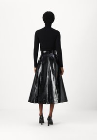 Top de cuello alto negro y una falda larga, de cintura alta, brillante con un patrón de serpiente negro. La falda tiene un diseño acampanado y se combina con tacones negros.