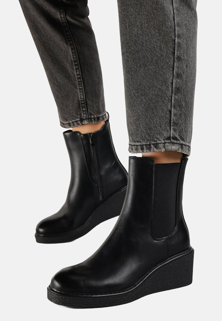 Bottines noires en cuir lisse avec un semelle en wedge. Elles sont dotées de panneaux élastiques sur les côtés et d'une fermeture éclair sur le côté, posées sur un jean gris.