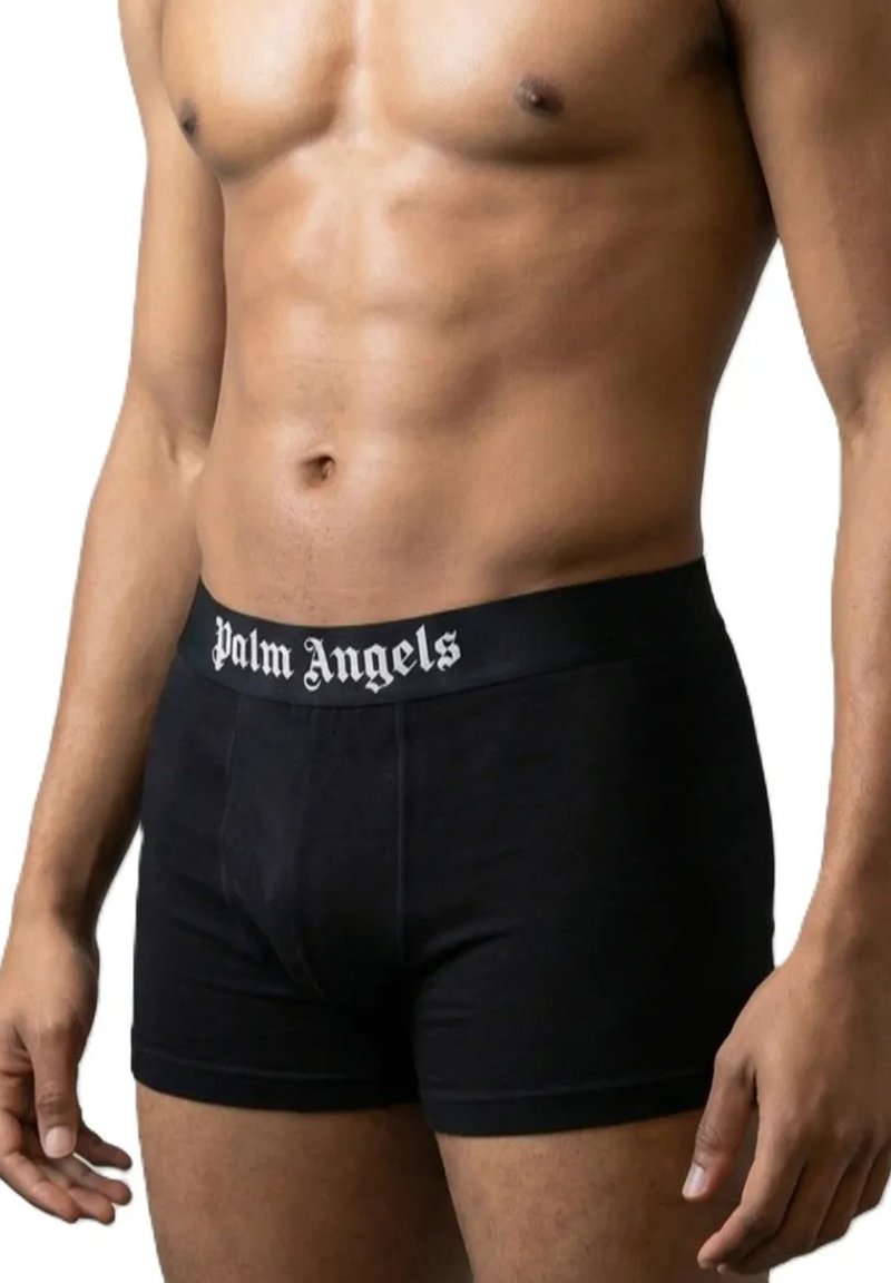 Ανδρικός κορμός που φοράει μαύρο εσώρουχο Palm Angels με ορατούς κοιλιακούς μύες και τα χέρια ακουμπούν στα πλευρά.