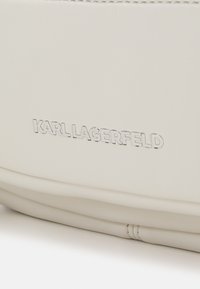 Balta oda gaminys su įspaustu "KARL LAGERFELD" logotipu sidabro spalva. Lygus paviršius su subtiliu siuvimo detalumu krašte.