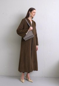 Pruun villane jakk laia varrukaga, pikk siluett, kombineeritud mustrilise käekoti ja kreemjate kontsadega. Minimalistlik disain, sile tekstuur.