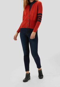 Red cardigan with black stripes on sleeves, featuring buttons. Paired with dark blue skinny jeans and black ankle boots with studs.