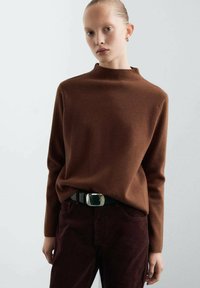 Pull à col montant marron en tissu doux, associé à un pantalon bourgogne foncé et une ceinture noire avec une boucle rectangulaire en argent.