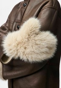 Brązowa skórzana kurtka z miękkim, jasnobeżowym akcentem z sztucznego futra na rękawie, charakteryzująca się puszystą teksturą i zaokrąglonym kształtem.