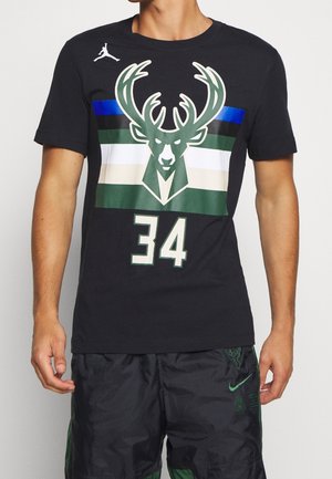 Homme portant un t-shirt noir des Milwaukee Bucks avec un grand logo de cerf, le numéro 34, et un short noir assorti avec un logo Nike vert.